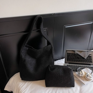 Vue détaillée d'un sac cabas noir en peluche avec sa pochette zippée sur un lit blanc