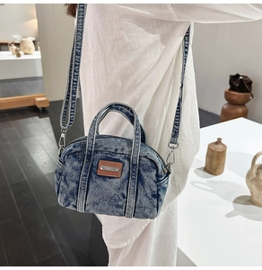 Detailed shot of a blue denim crossbody bag with leather trim on a white shirt model