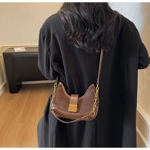 Detail view of the brown leather baguette bag showing texture contrast and golden metal buckle