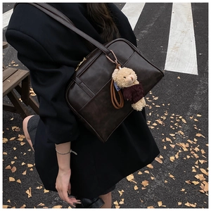 Detailaufnahme der tiefbraunen Boston-Tasche mit Teddybär-Anhänger auf Herbststraße