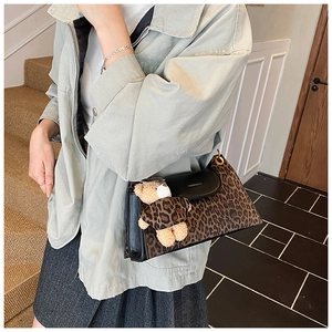 Detail of leopard print suede shoulder bag with matte black flap and plush bear charm