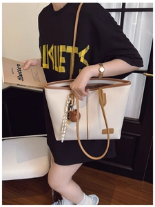 Close-up of cream tote bag with brown leather trim and cute bear charm accessory
