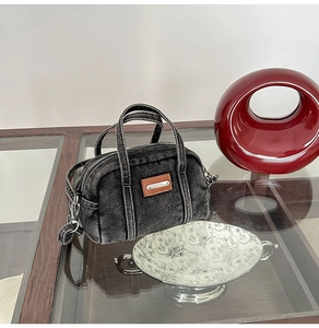 Detail of dark gray denim cylinder bag featuring contrast stitching and logo plate