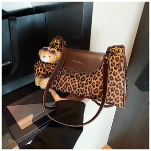 Detail of leopard print handbag featuring a plush bear charm and brown leather strap