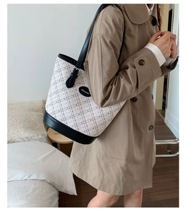 Detail view of stylish white checkered bucket bag with black leather trim worn by model