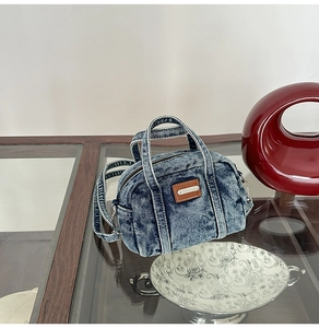 Detail of blue washed denim mini bowling bag with white stitching and brand patch