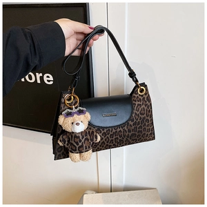 Detail of leopard print handbag featuring black leather flap and cute bear charm accessory
