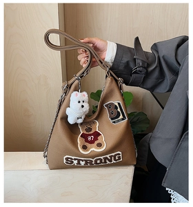 Dettaglio borsa tote marrone con ricamo di orsetto, lettera B e ciondolo cane di peluche