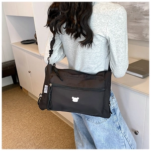 Détail du sac bandoulière en nylon noir avec bandoulière plissée et écusson d'ours