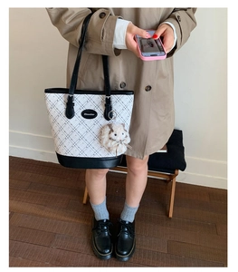 Close-up of quilted tote bag with rabbit charm, styled with a khaki trench coat