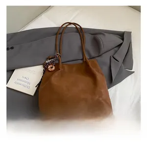 Close-up of brown suede tote bag with logo embossing and stylish charm on grey suit jacket
