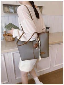 Detail of grey pebble leather tote bag with brown trim and plush bear charm on shoulder