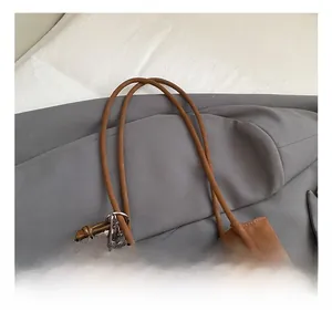 Macro detail of tan leather tote bag featuring a 2DN logo and woven donut charm pendant