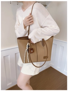 Close-up of khaki tote bag featuring litchi texture and a cute bear bag charm