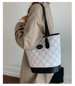 Detail of patterned white tote bag with black trim worn with a beige trench coat