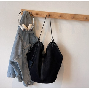 Macro detail of minimalist black suede hobo bag hanging with a denim jacket and headphones