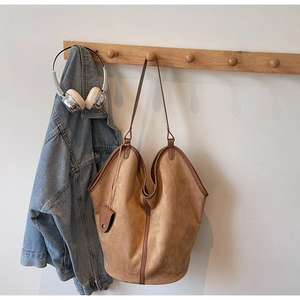Close-up of tan suede tote bag with small pouch hanging on a wooden coat rack