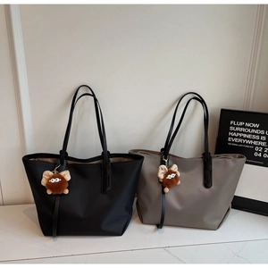 Détail des sacs cabas noir et marron avec anses en cuir et breloques de monstres en peluche