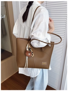 Detail view of brown pebbled leather tote bag with cute bear charm and logo patch