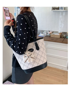 Detail of cream quilted tote bag with black trim and plush doll charm on model