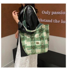 Detail of green plaid plush tote bag with metal emblem and wide shoulder strap