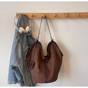 Detail of coffee suede tote bag hanging on wooden hook with casual lifestyle props