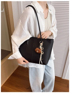 Detail of black pebbled leather tote bag with bear charm and bicolor chain strap