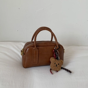 Detailansicht der braunen Bowlingtasche mit Teddybär-Anhänger auf weißem Tuch