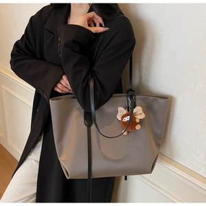 Détail du grand sac cabas en cuir gris avec bandoulière noire et breloque peluche sur blazer