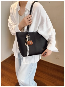 Detail of black pebbled leather tote bag with a brown bear charm and decorative chain