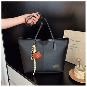Detail of black pebbled leather tote bag with bear charm and chain decoration
