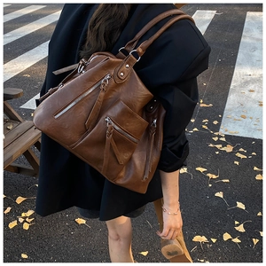 Detail view of brown PU leather shoulder bag with tassels and multiple zipper pockets