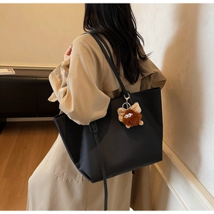 Vue latérale du grand sac cabas noir minimaliste avec charm monstre en peluche sur l'épaule