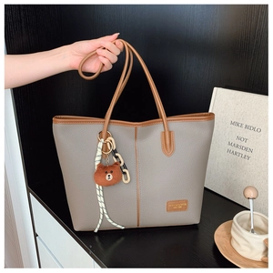 Detail shot of taupe pebbled leather tote bag with brown straps and cute bear keychain charm