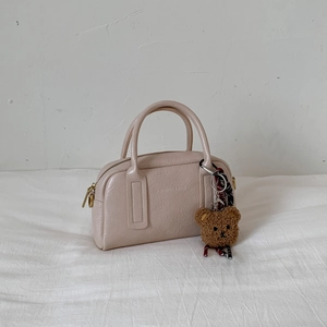 Detailansicht der cremefarbenen Boston-Tasche mit Lederstruktur und Bärenanhänger