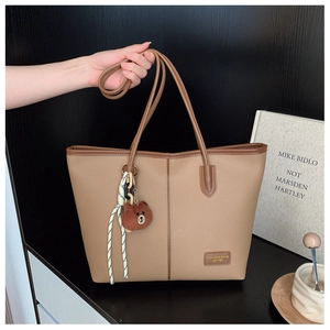 Detail of minimalist tote bag in pebbled leather with cute plush bear pendant accessory