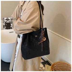 Detail of black suede tote bag showing the gold logo and knotted rope pendant decoration