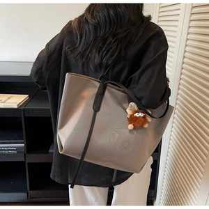 Détail du sac fourre-tout gris kaki avec lanières noires et pendentif en peluche marron