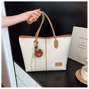 Detail of white lychee leather tote bag with brown straps and cute bear charm decoration