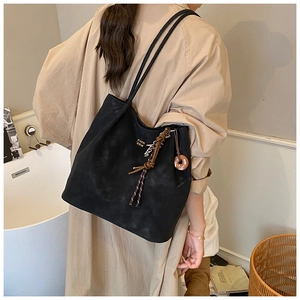 Detail view of large black suede tote bag with braided knot accessory and logo printing