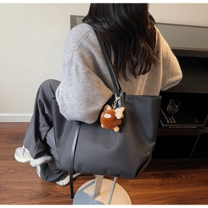 Détail macro du sac cabas en nylon noir avec un pendentif poupée en peluche marron