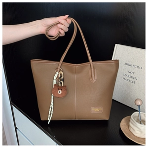 Detail of vintage brown leather tote bag with vertical stitching and cute bear charm