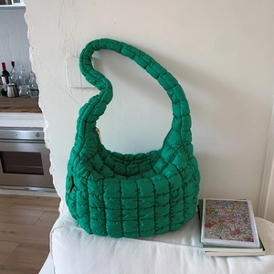 Detail of a shiny green quilted bubble cloud bag with soft nylon texture and padded strap