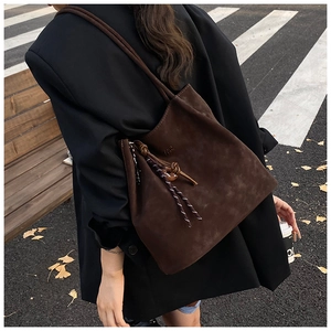 Detail of dark brown suede tote bag featuring a knotted rope charm in a street setting