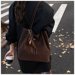 Detailed close-up of brown suede tote bag with woven knots and golden letter charm