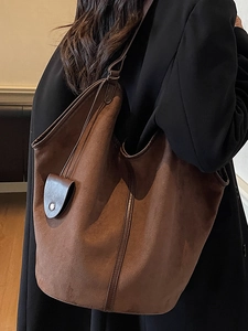 Retro brown oversized suede hobo tote bag with slim straps worn by a model in black coat
