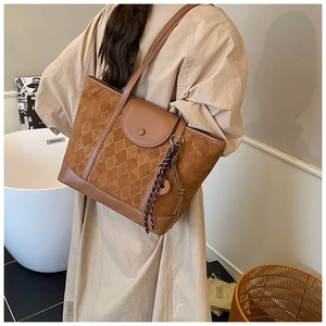 Detail of dark brown quilted tote bag with textured finish and woven charm accessory