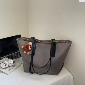 Détail du sac cabas gris brun avec de fines anses noires et un charme en peluche