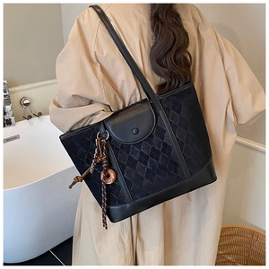 Detail of black quilted tote bag with smooth leather trim and woven cord pendant