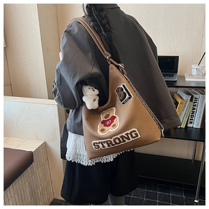 Dettaglio di una borsa tote marrone con ricamo a orsetto e portachiavi in peluche bianco